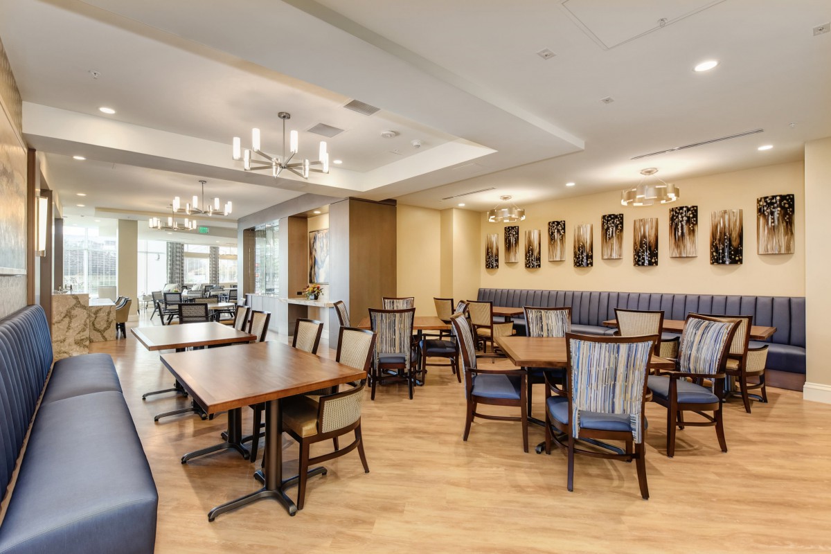 A modern dining area with neatly arranged tables and chairs, featuring elegant chandeliers and a wooden floor.
