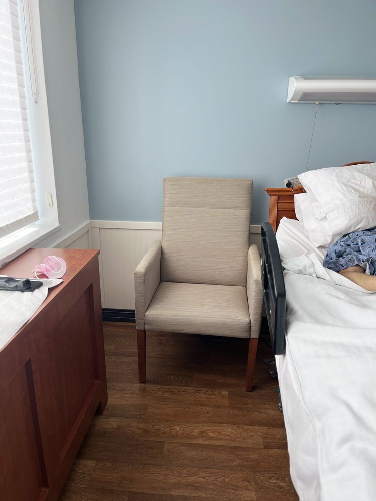 A hospital room with a beige chair beside a bed and window.