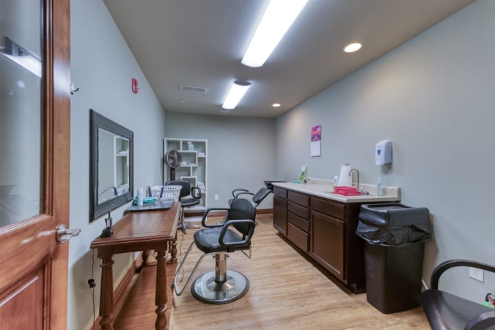A small hair salon with a styling chair, mirror, and counter in a well-lit room.