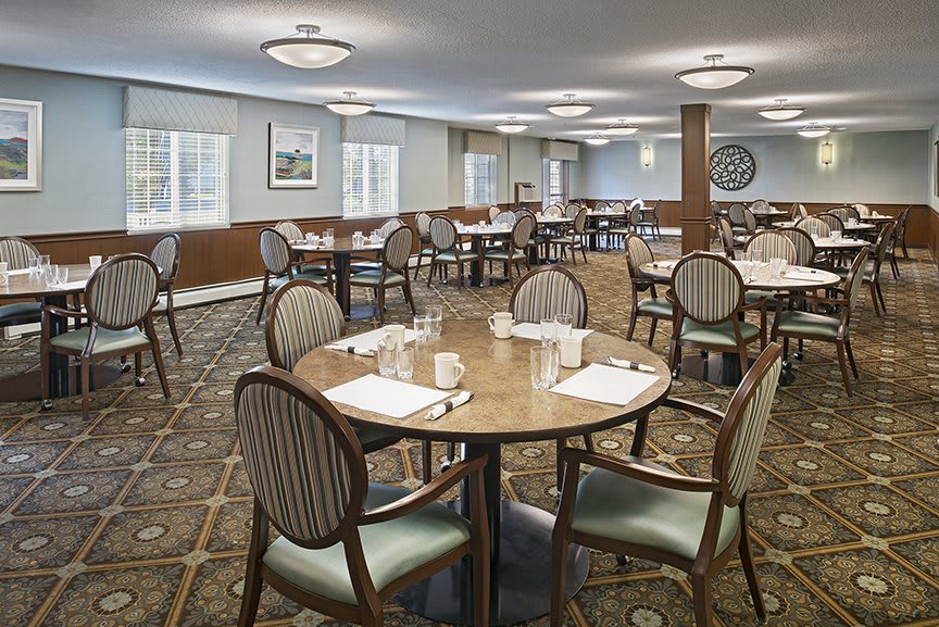 An elegantly set dining room with round tables and cushioned chairs.