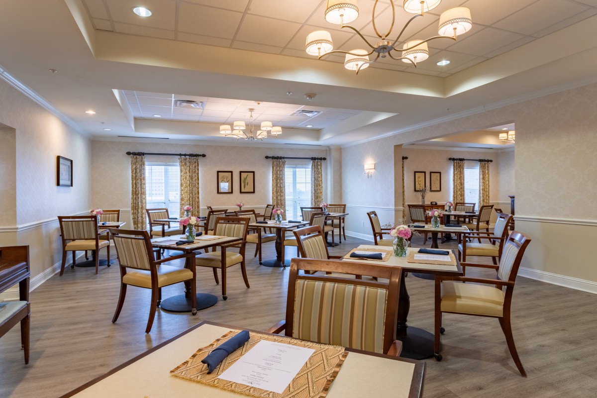 A spacious and elegantly decorated dining room with multiple tables and chairs, well-lit by chandeliers.