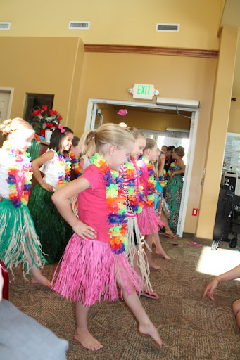 Children performing a hula dance in colorful costumes with leis.