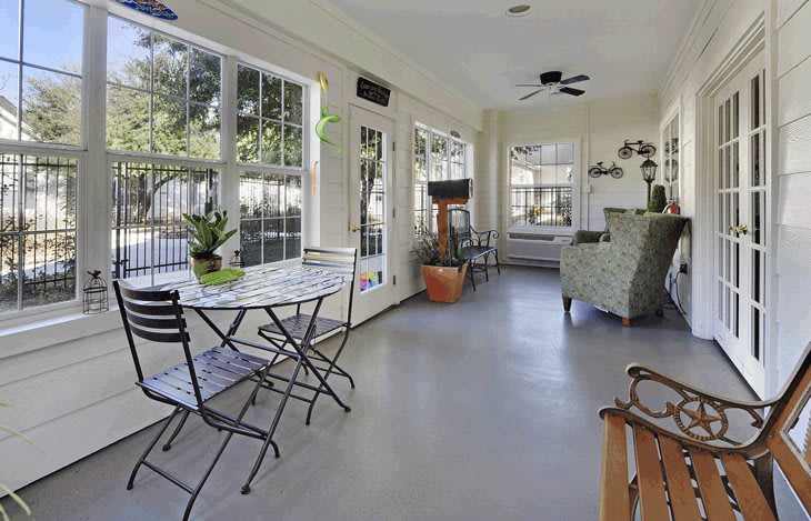 A bright sunroom with large windows, featuring a seating area and potted plants.