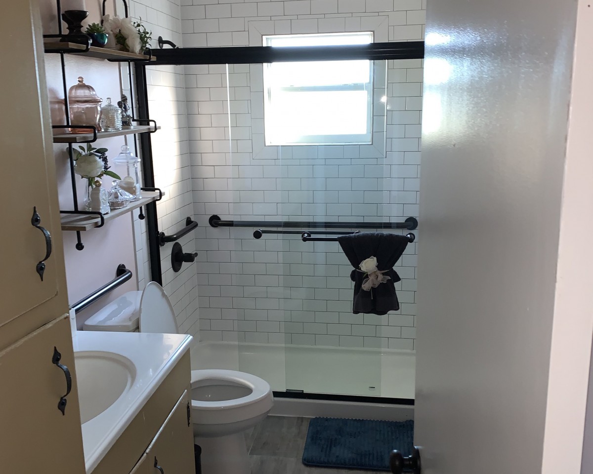 A modern bathroom with glass shower doors, white tiles, and black fixtures.