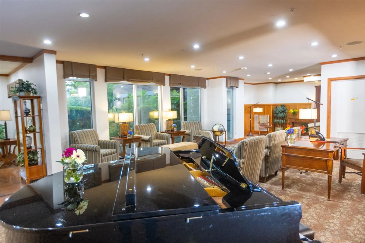 A spacious and modern living room featuring a grand piano, comfortable seating, and large windows.