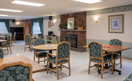 A cozy common room featuring tables and chairs arranged around a fireplace, creating a welcoming atmosphere.