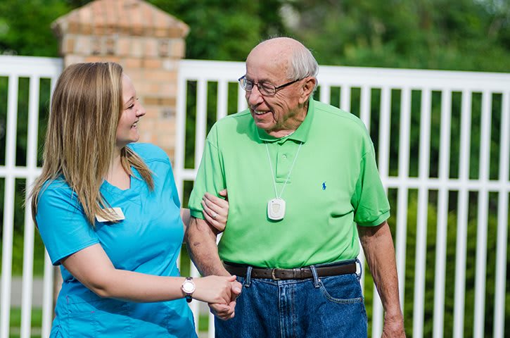 A caregiver assists an elderly man outdoors, providing support and companionship.