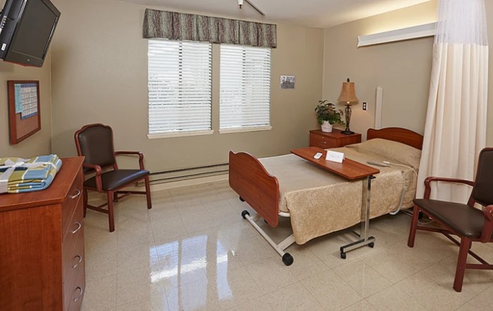 A tidy hospital room featuring a bed, chair, side table, and window with curtains.