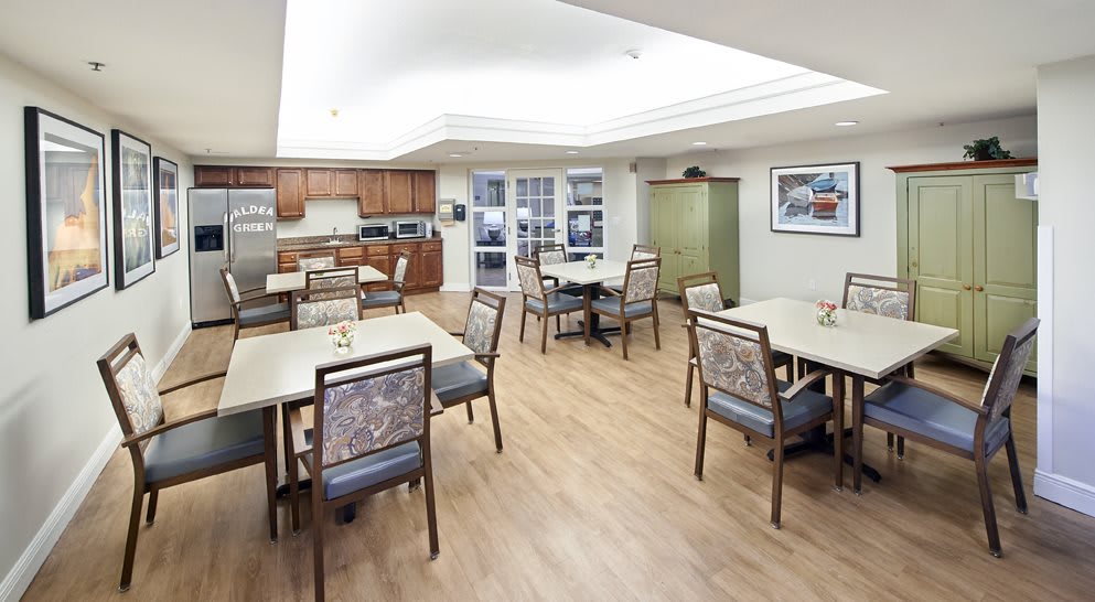 A spacious dining area with multiple tables and chairs, featuring a wooden floor and an adjoining kitchen.