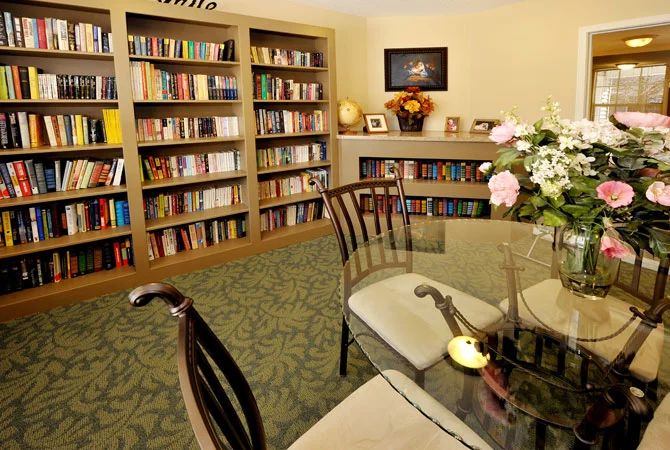 A cozy indoor library with bookshelves, a glass table, and chairs surrounded by decorative elements.