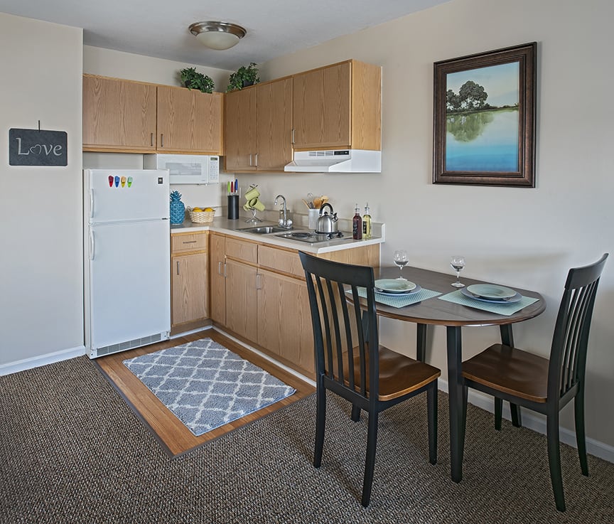 A cozy kitchen with a small dining area, featuring wooden cabinets, a refrigerator, and a neatly set table.