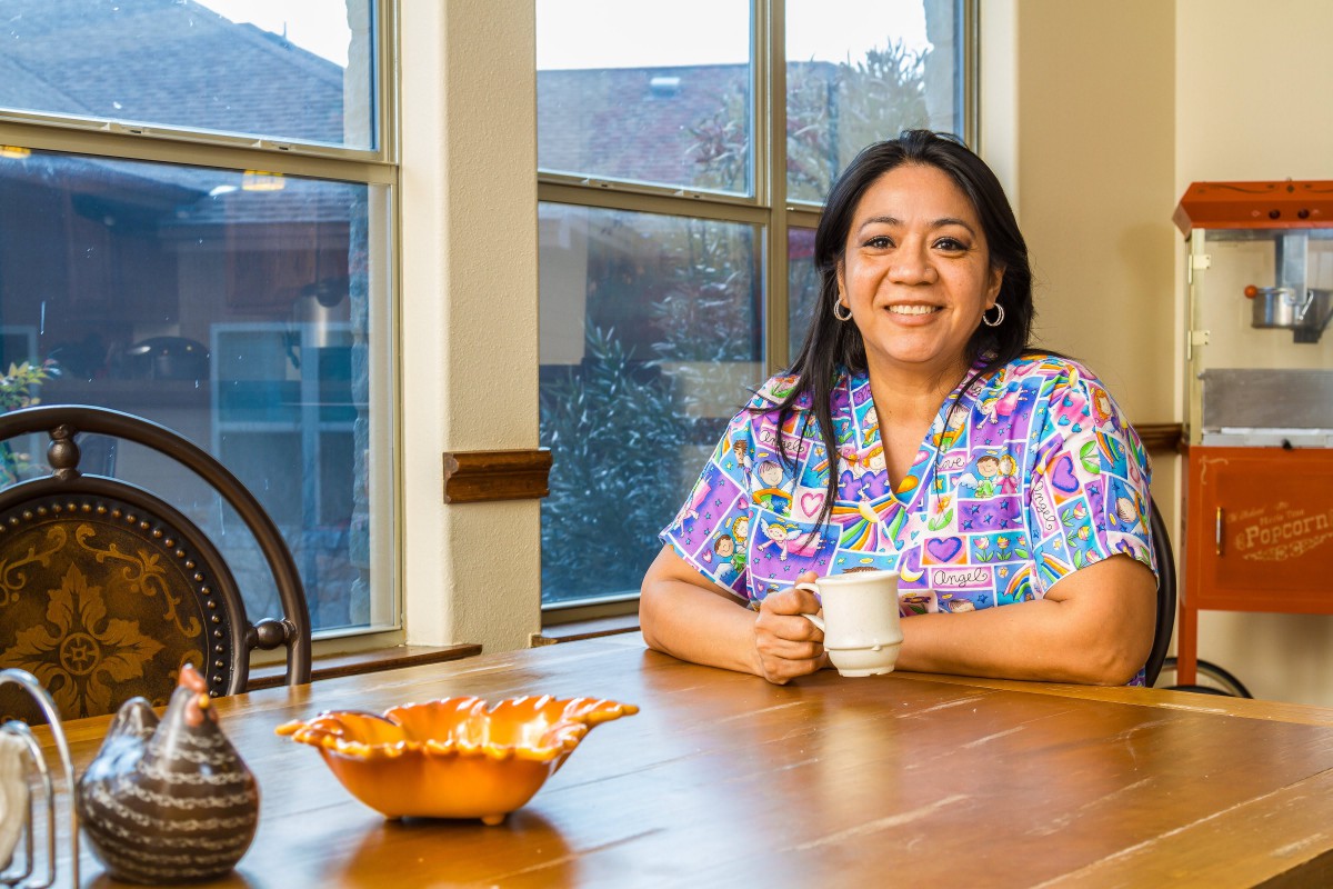A woman smiling while sitting at a kitchen table with a coffee cup.