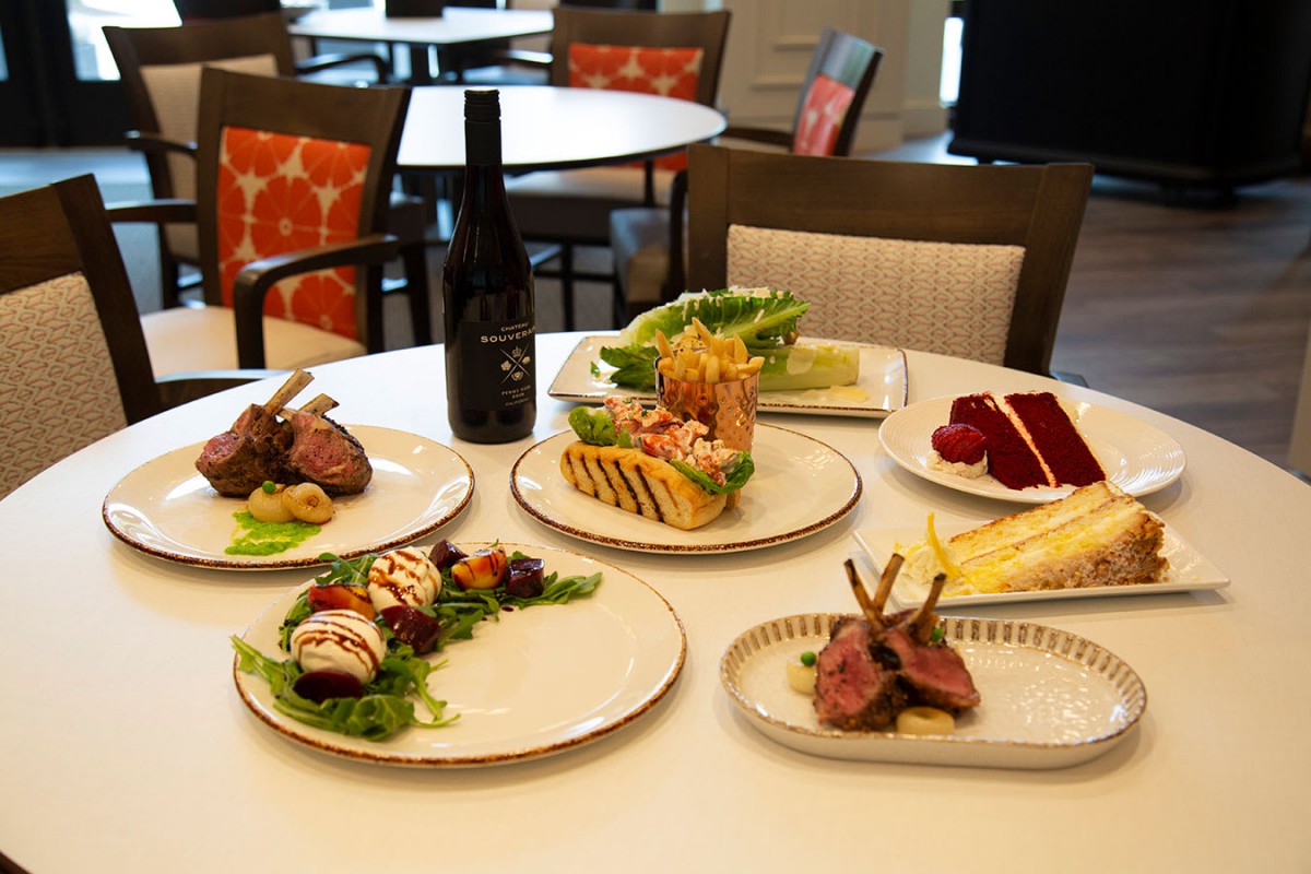 A gourmet dining setup featuring lamb chops, desserts, and a bottle of wine on a restaurant table.