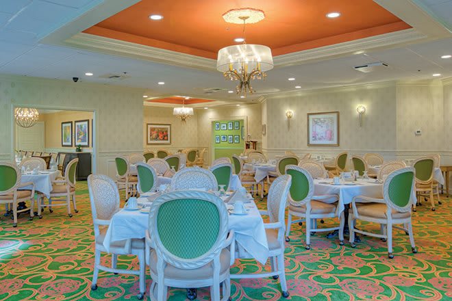 An elegant restaurant dining room with green and white furniture and a chandelier.
