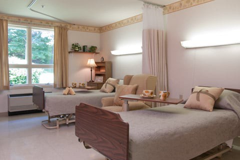 A well-lit hospital room with two beds separated by a curtain, featuring a light and calming interior design.