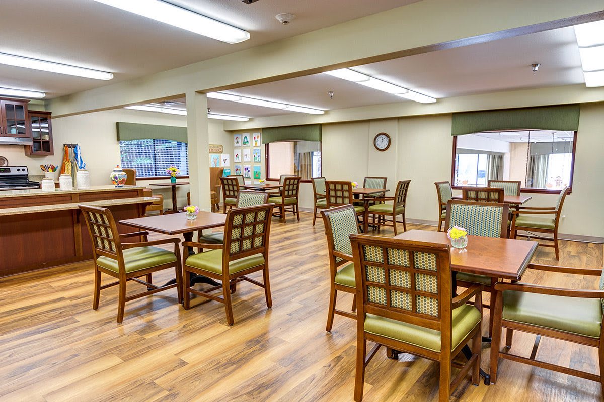 A spacious and well-lit dining area with wooden floors, featuring neatly arranged tables and chairs.