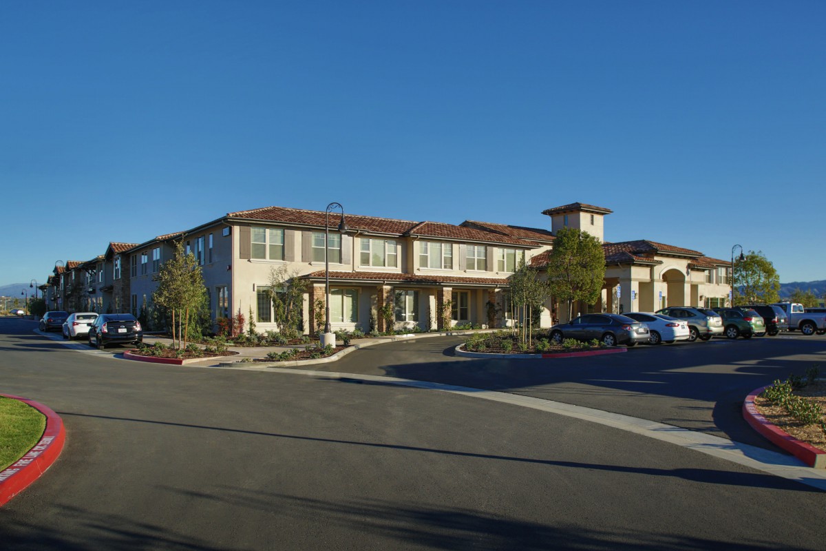 A large, two-story building with a parking lot in front, set against a clear blue sky.
