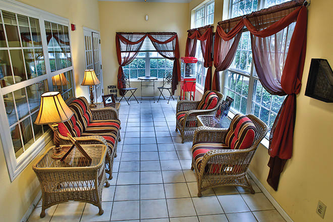 A cozy sunroom featuring wicker furniture, large windows with curtains, and ambient lighting.