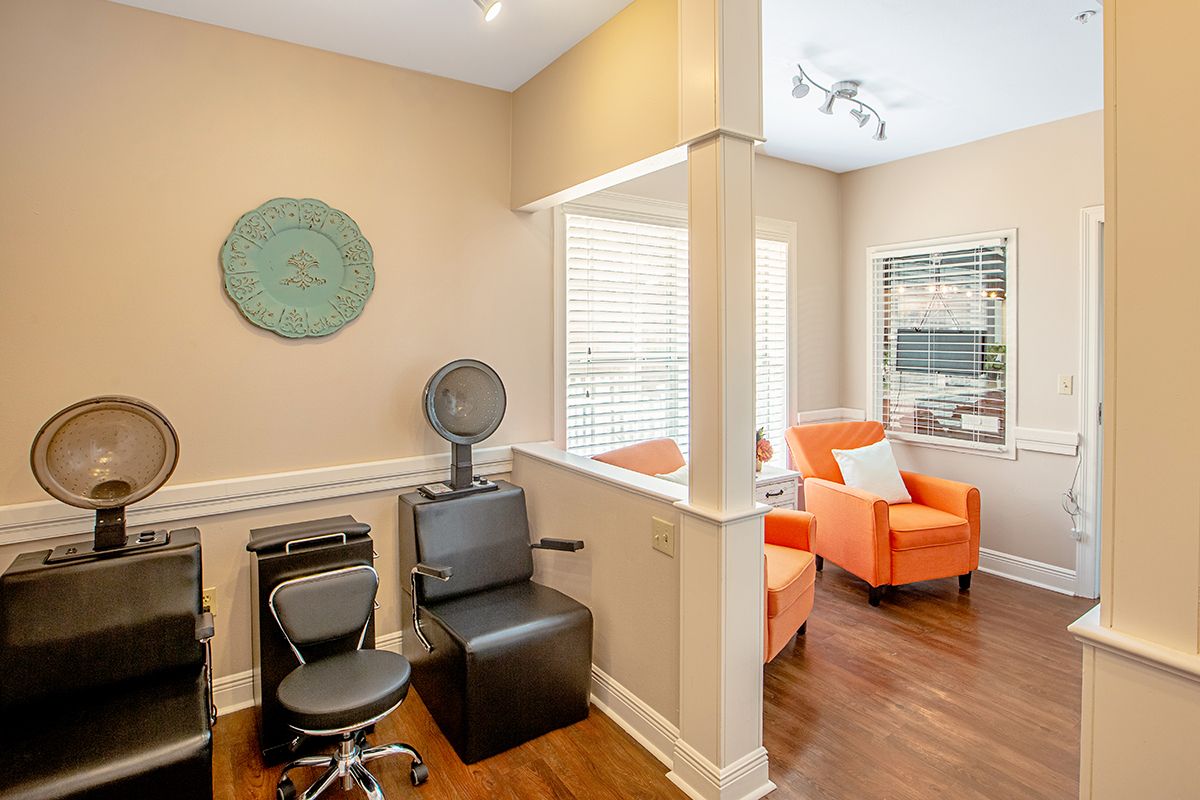 A modern salon with a hair drying station and a cozy waiting area featuring bright orange chairs.