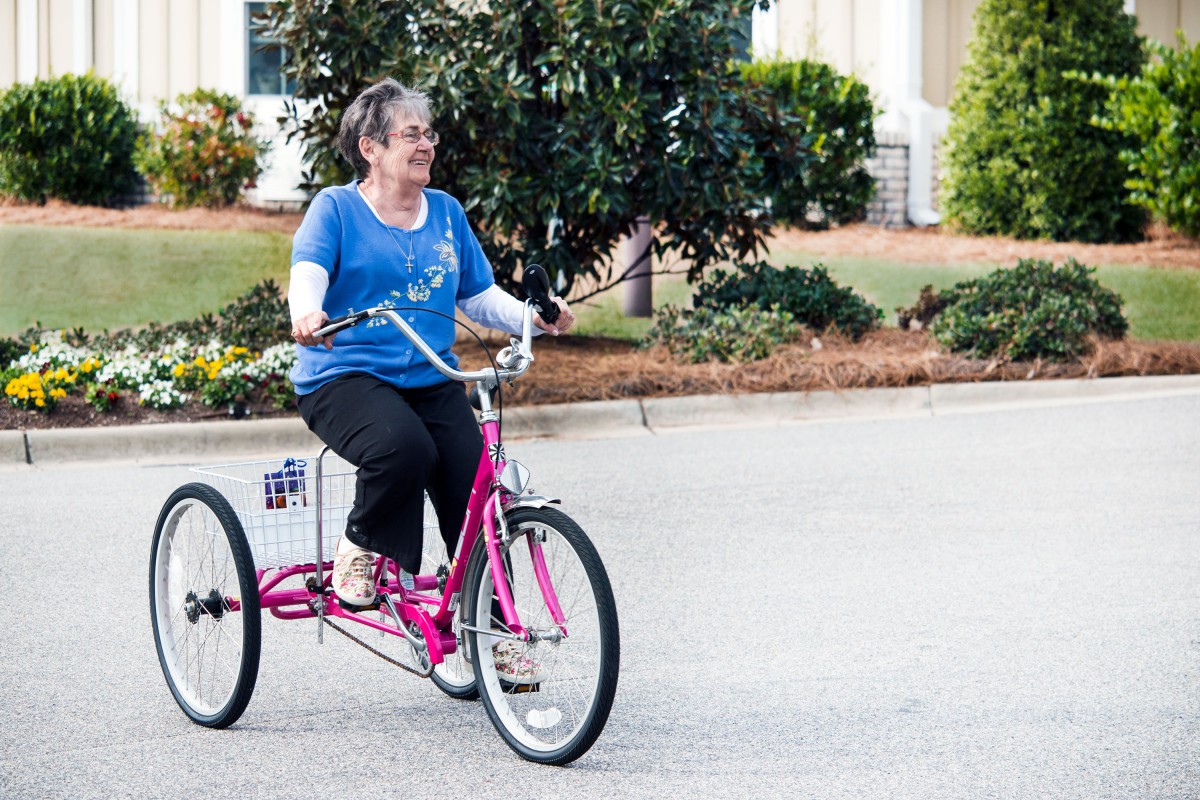 A woman enjoying a ride on a pink tricycle outdoors.