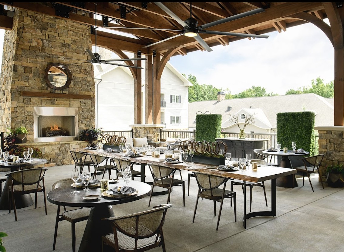 An elegantly set outdoor dining area with neatly arranged tables and chairs under a wooden roof, offering a cozy ambiance.