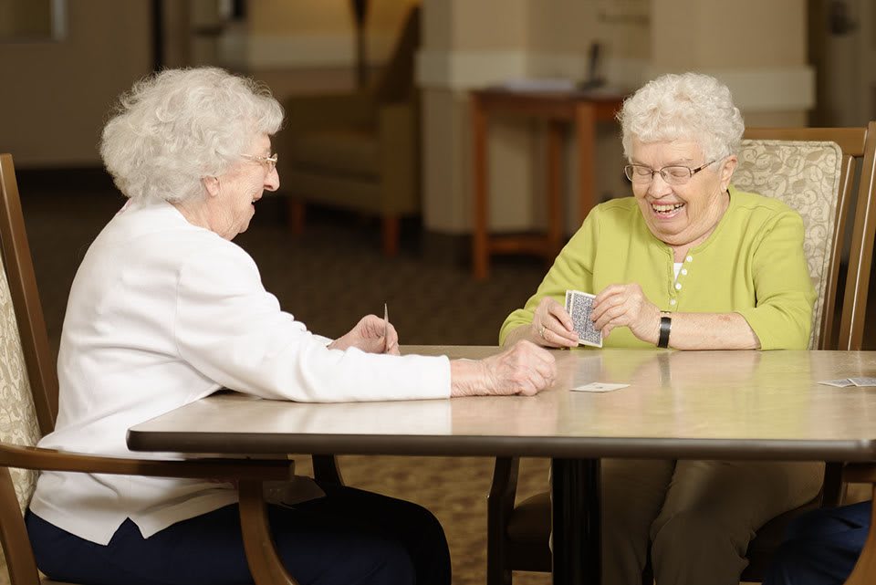 Two elderly women enjoying a game of cards together indoors.