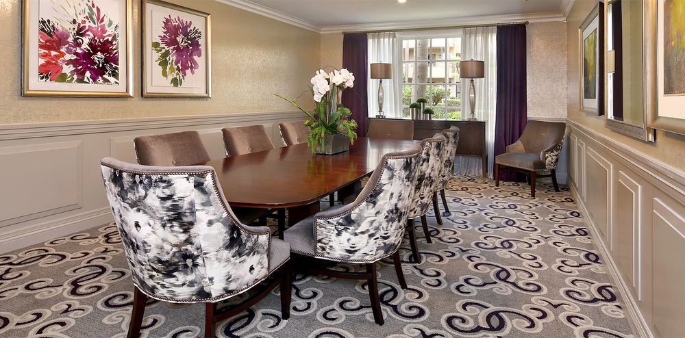 A well-designed dining room featuring a long table with upholstered chairs, a decorative carpet, and elegant floral arrangements.