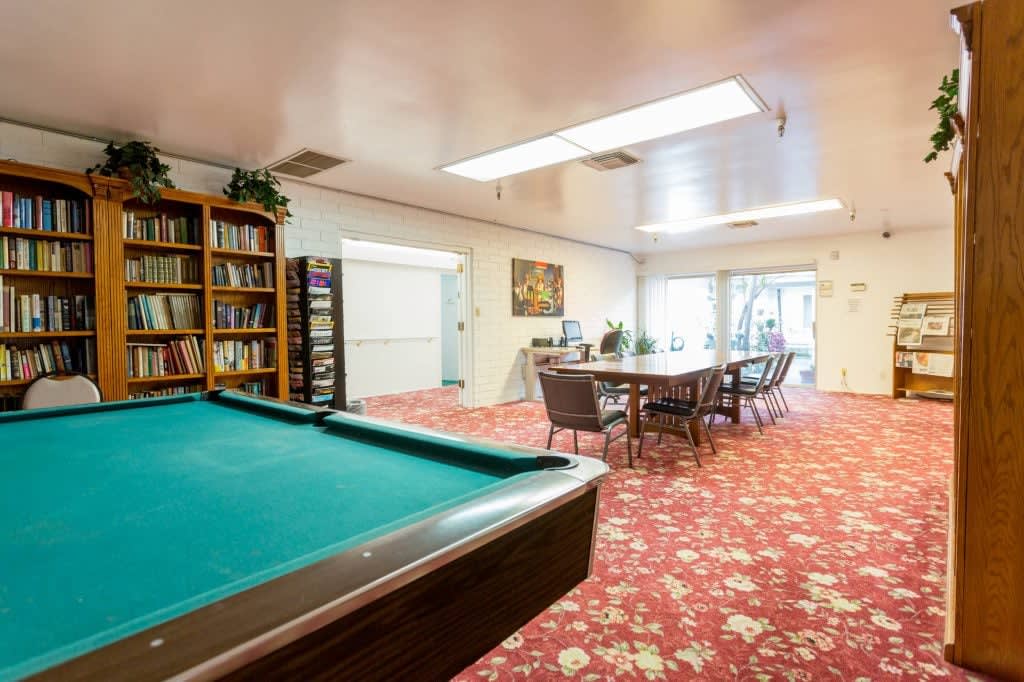 A cozy recreation room featuring a pool table, bookshelves, and a large dining table with floral carpeting.