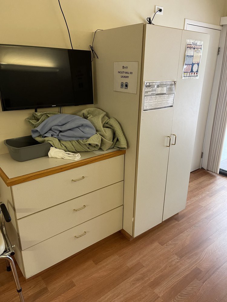 A medical room with a monitor above a set of drawers, clothes on the counter, and a cabinet nearby.
