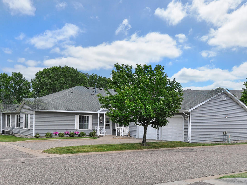 A suburban house with a driveway and garage, surrounded by greenery under a partly cloudy sky.