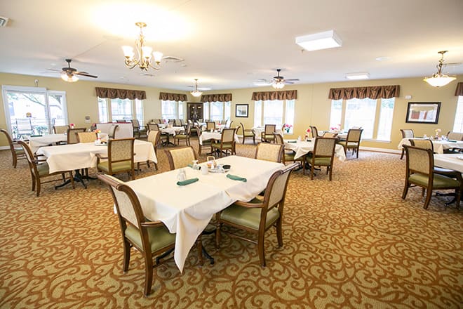 A spacious dining room with several tables and chairs, elegant decor, and well-lit chandeliers.