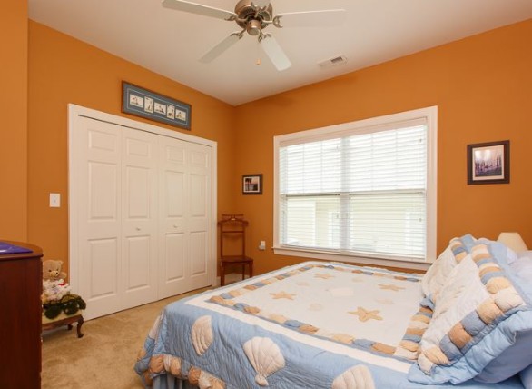 A cozy bedroom with orange walls, featuring a ceiling fan and a window providing natural light.