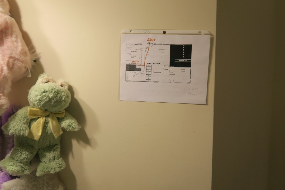 A teddy bear hangs on a wall next to a paper with a floor plan.