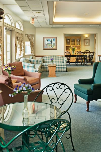 A cozy living room with various chairs, a sofa, and a glass table featuring a vase with flowers.