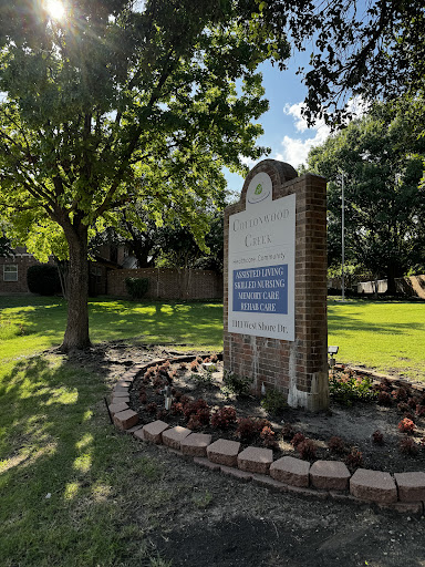 A welcoming sign set in a lush green landscape with trees and well-maintained flower beds.