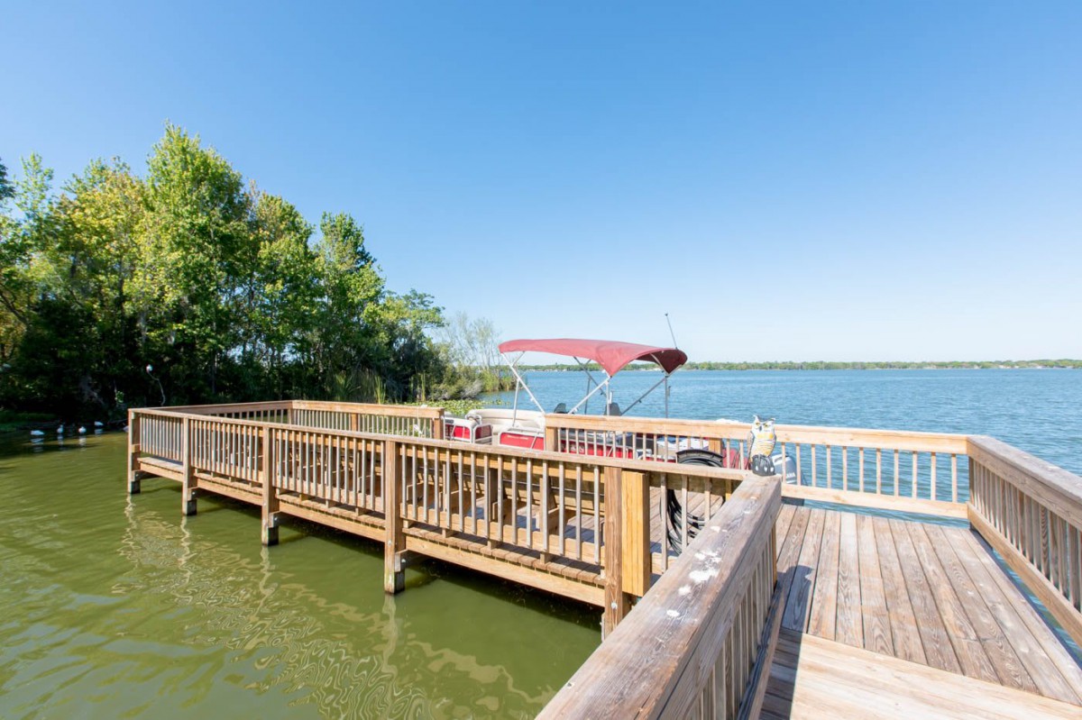 A wooden dock with a boat on a tranquil lake surrounded by trees under a clear blue sky.