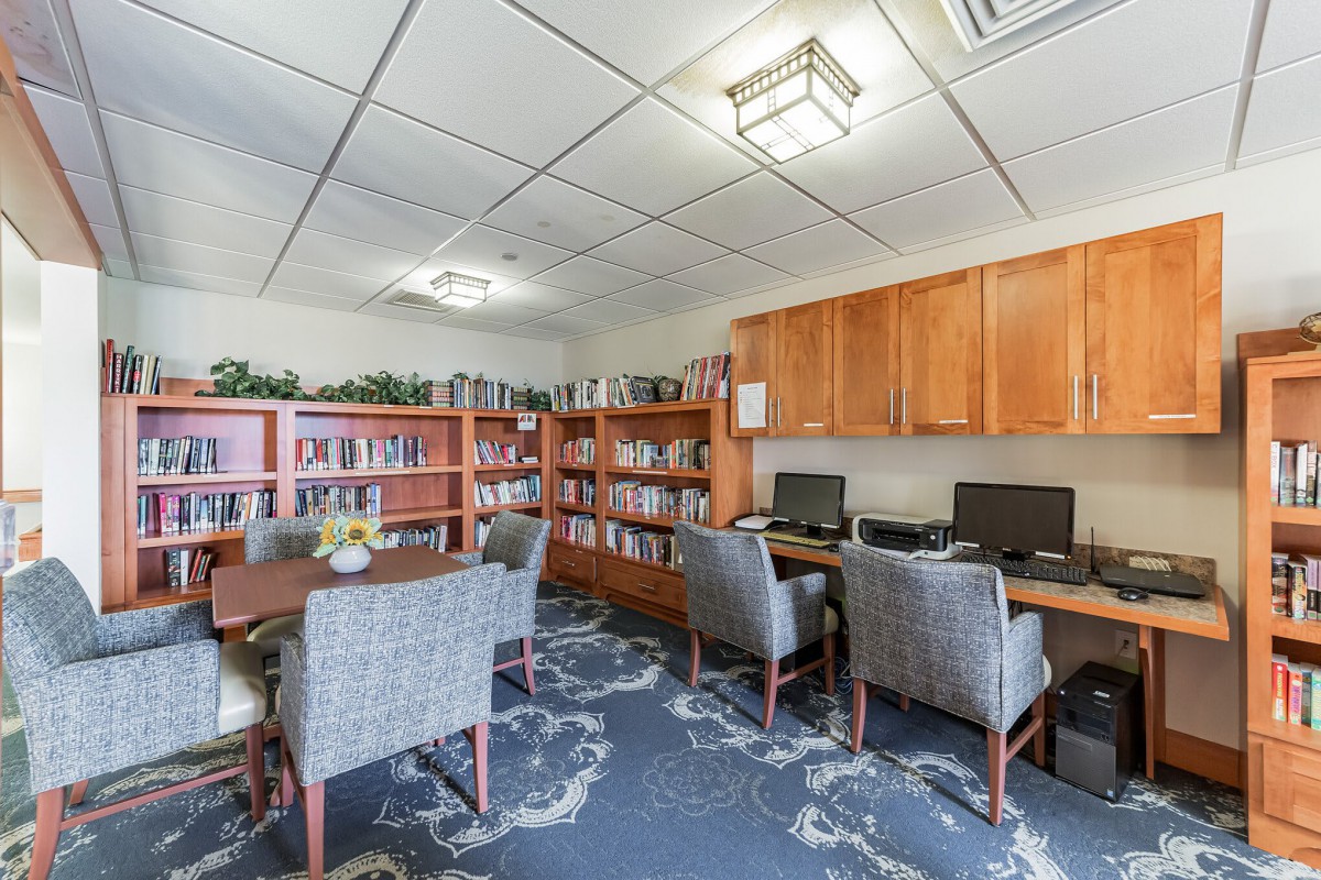 A cozy office space featuring bookshelves, computers, and seating for meetings.