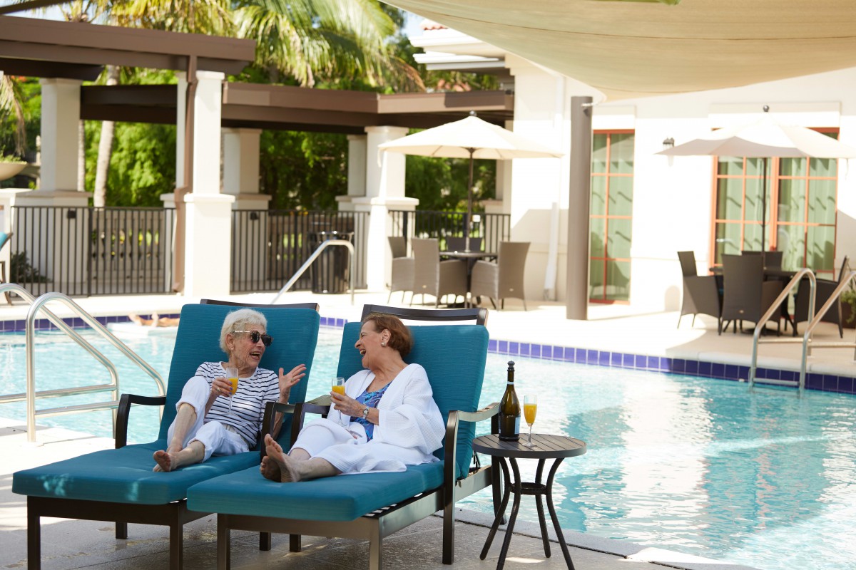 Two people relaxing and chatting poolside on lounge chairs.