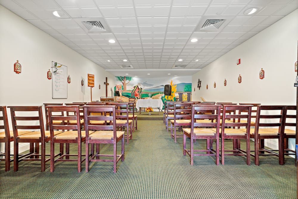 A well-lit room with rows of wooden chairs and tables, featuring colorful artwork on the walls.