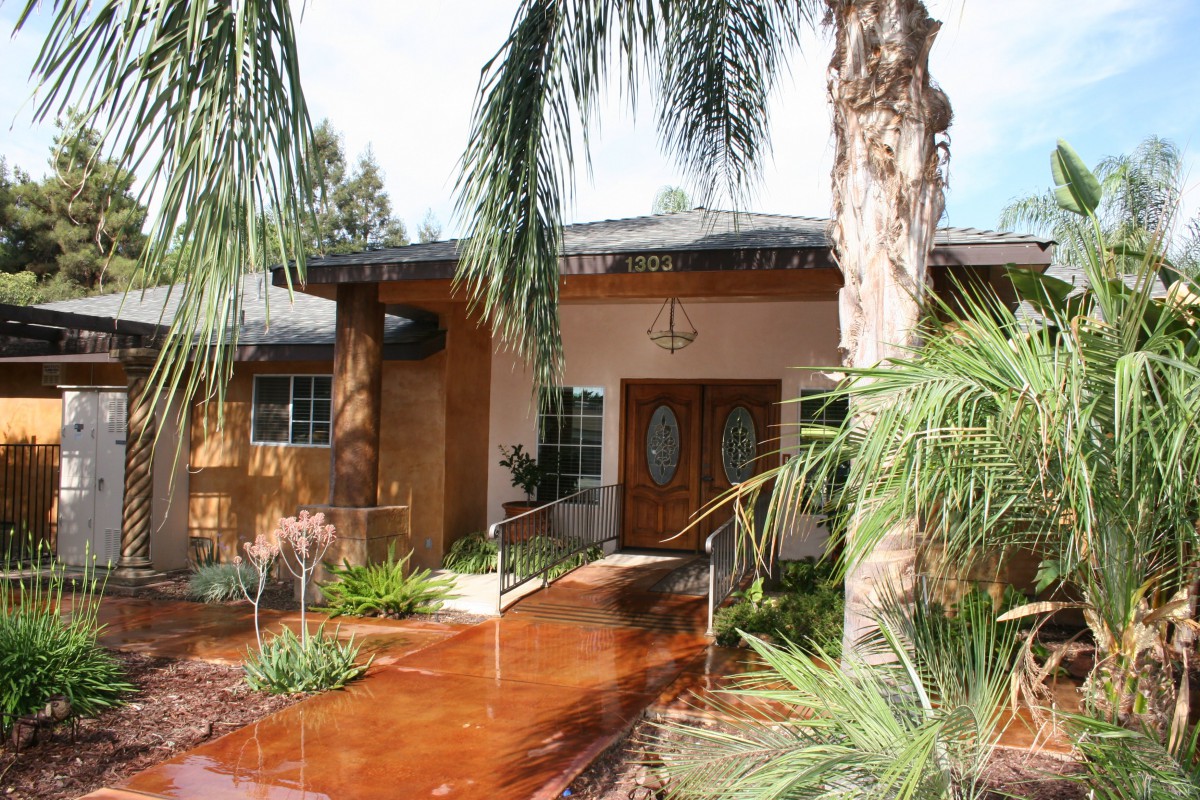 A welcoming house entrance surrounded by palm trees and lush landscaping.