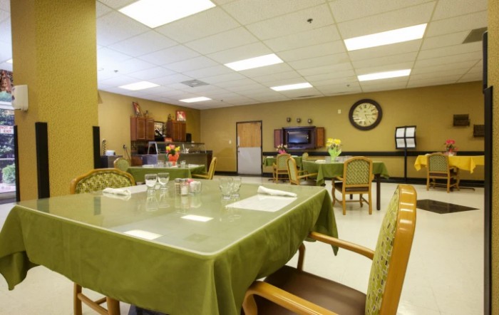An empty dining area with green tablecloths, a clock on the wall, and a television.