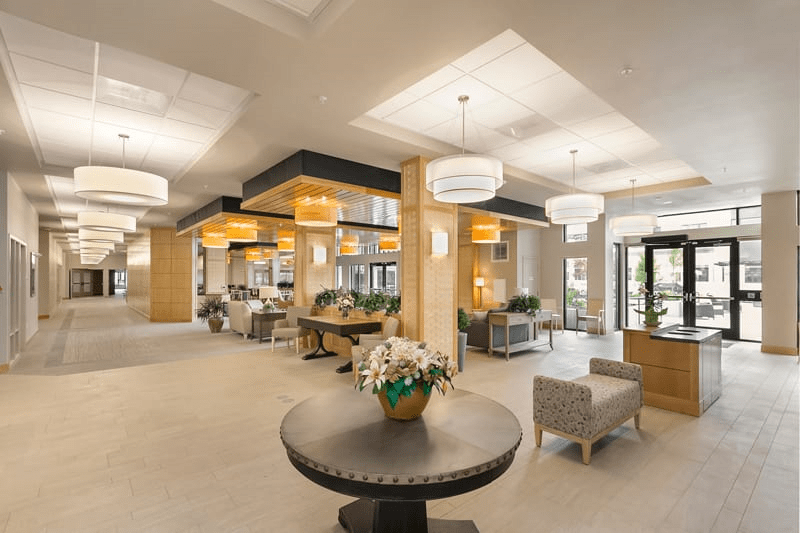 A modern lobby with elegant furniture and decorative lighting, featuring a central table with flowers.