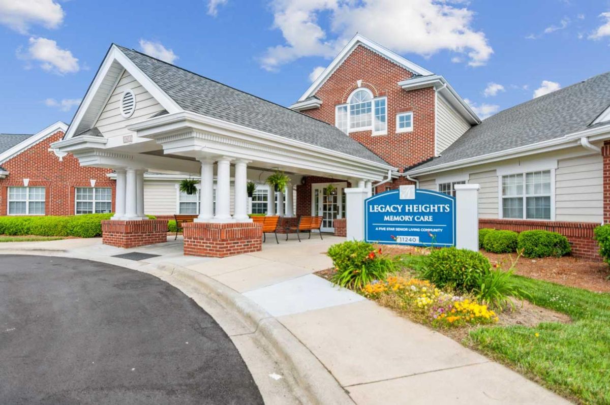 A welcoming entrance to a modern building with a sign, surrounded by well-maintained landscaping under a blue sky.