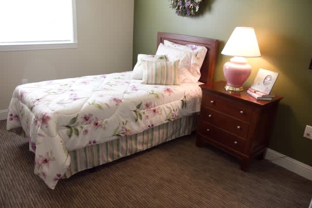 A cozy bedroom with a single bed adorned with floral bedding, a pillow, and a wooden nightstand featuring a lamp.