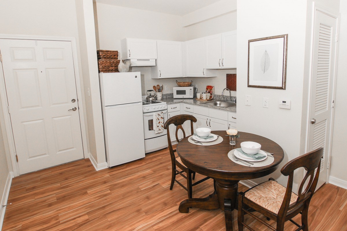 A cozy kitchen and dining area featuring a small round table set for two, with white cabinets and essential appliances.