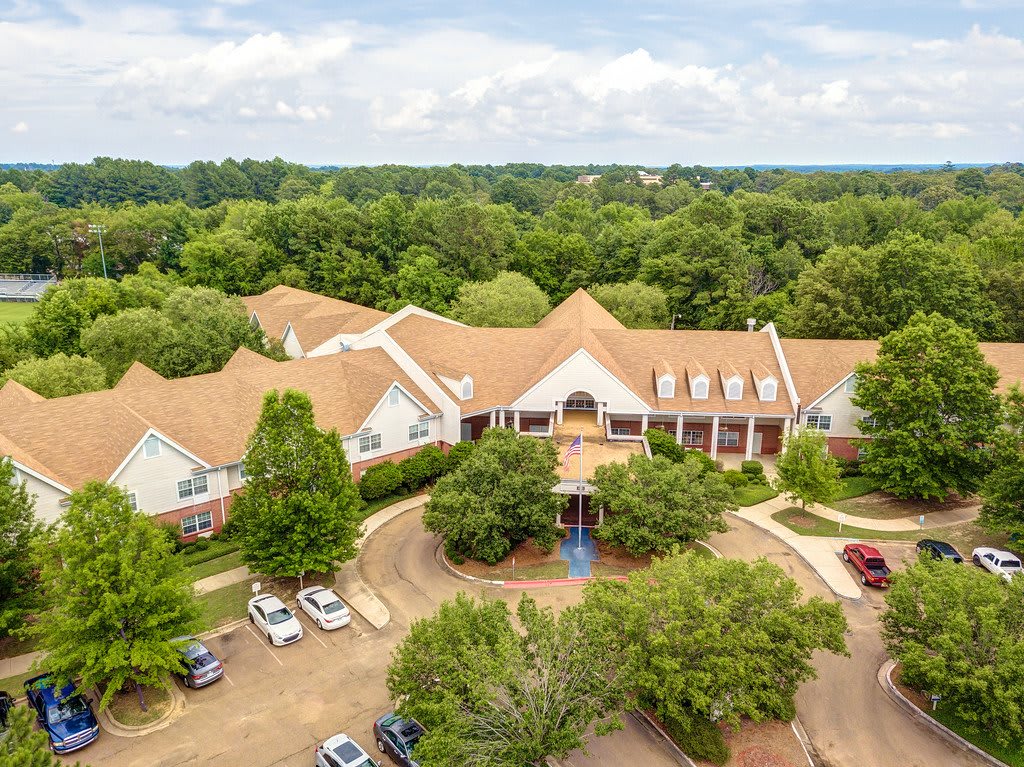 Aerial view of a large building surrounded by trees with a parking lot in front.
