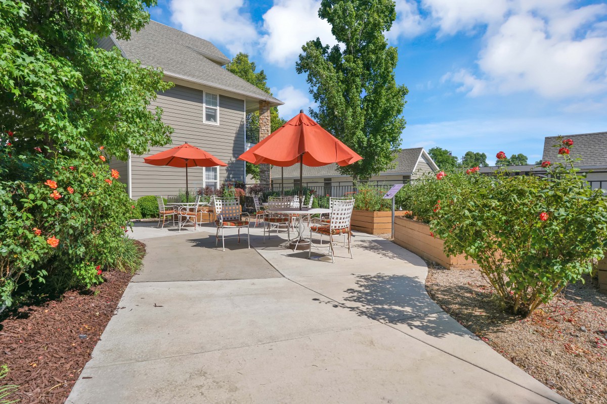 A sunny outdoor patio area with tables, chairs, and orange umbrellas next to a house.