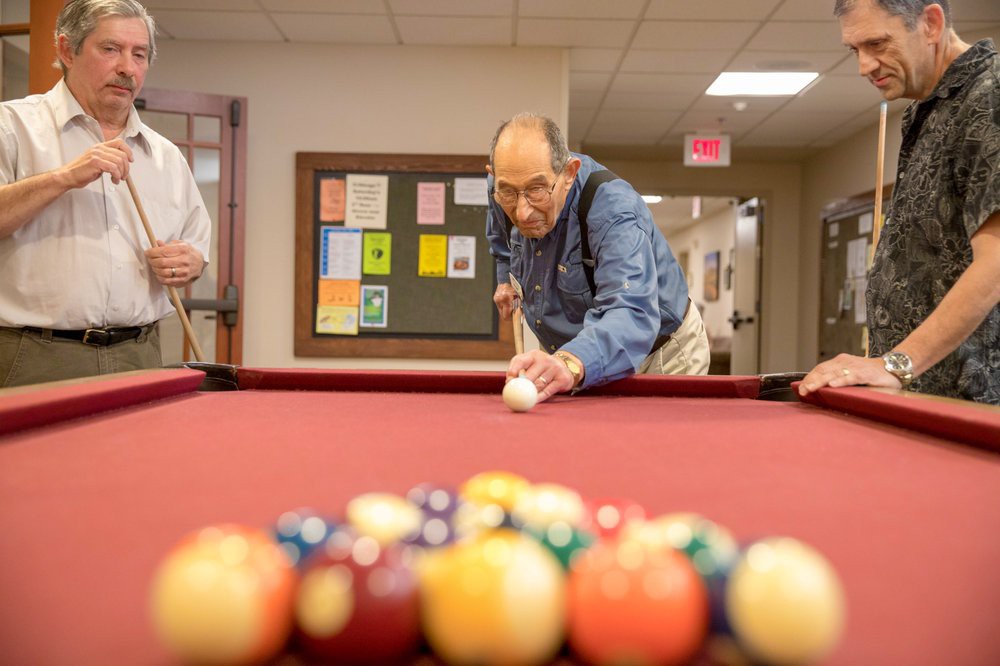 An elderly man focuses intently as he prepares to take a shot in a game of pool.