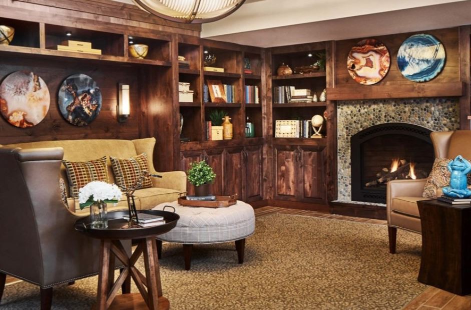 A cozy living room with wood paneling, bookshelves, and a fireplace.
