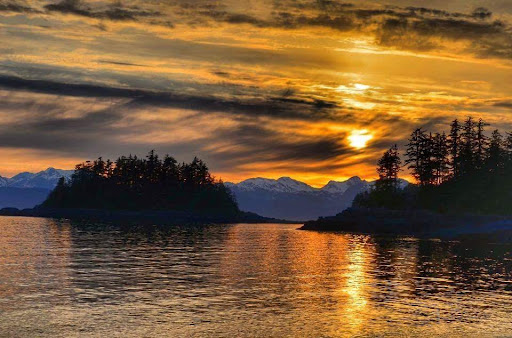 A breathtaking sunset casting golden hues over tranquil waters, framed by distant mountains.